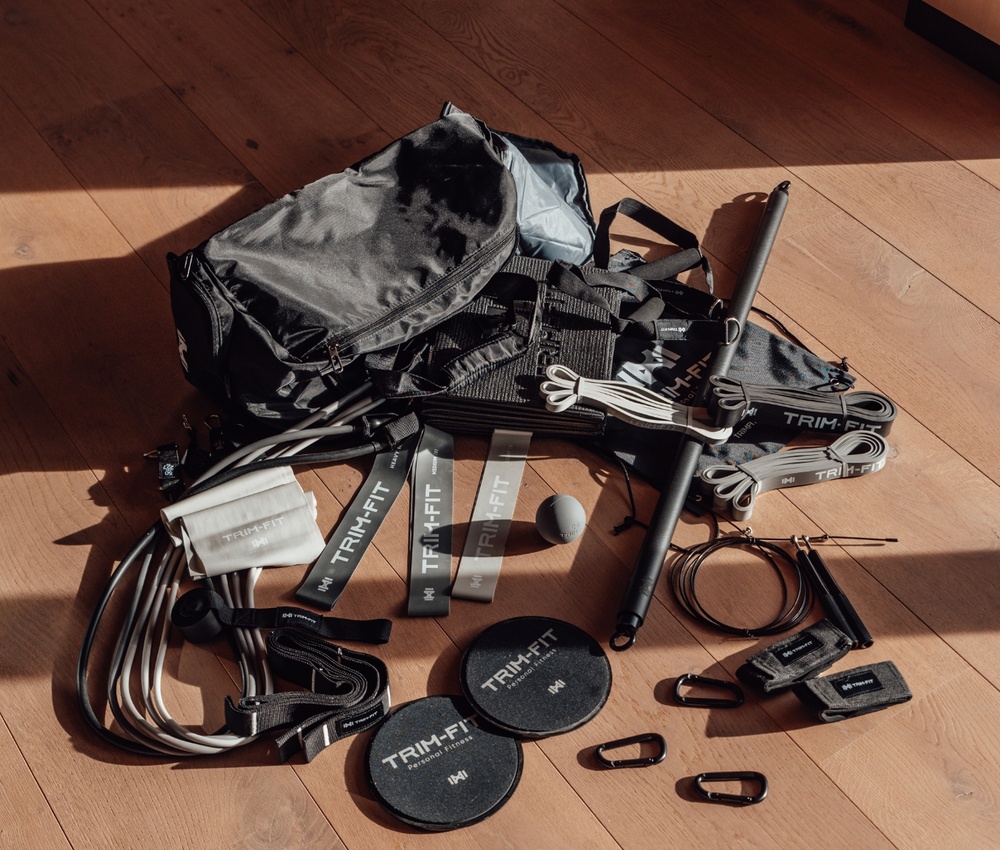 Eine Sporttasche mit Trainingsbändern, Gleitern, einem Springseil, Griffen und Karabinern auf einem Holzboden.