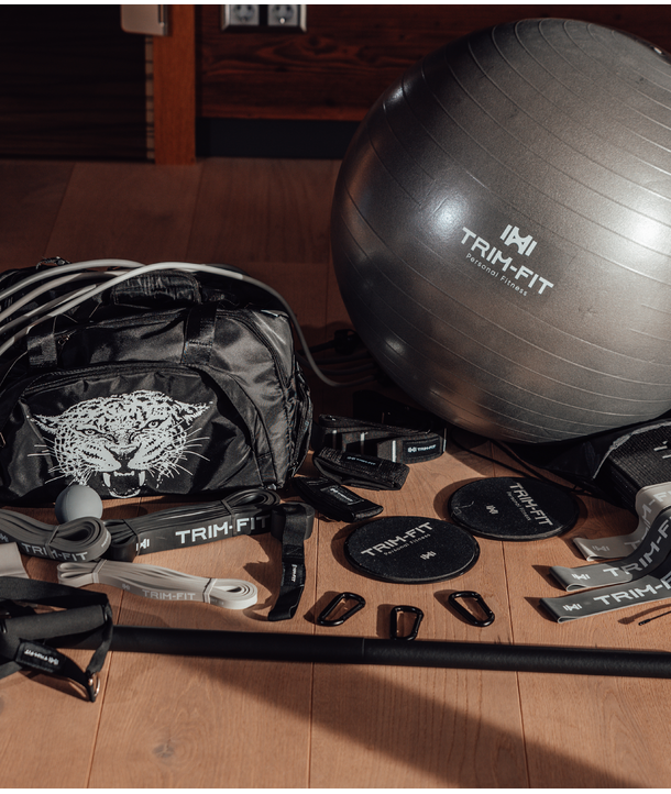 Fitnessgeräte, darunter ein Trim-Fit-Trainingsball, ein Beutel, Bänder, Schieber und Widerstandszubehör auf einem Boden.
