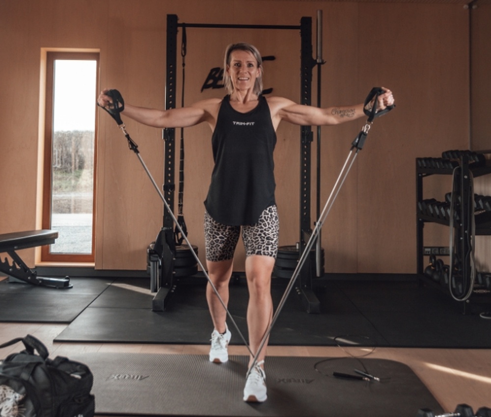 Frau, die in einem Fitnessstudio mit Widerstandsbändern trainiert, trägt ein schwarzes Tanktop und Shorts mit Leopardenmuster.