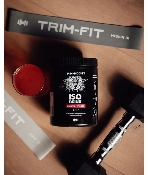 Schwarzer ISO-Drink-Behälter, Glas mit roter Flüssigkeit, Kurzhantel und Widerstandsbänder mit der Aufschrift TRIM-FIT auf einer Holzfläche.