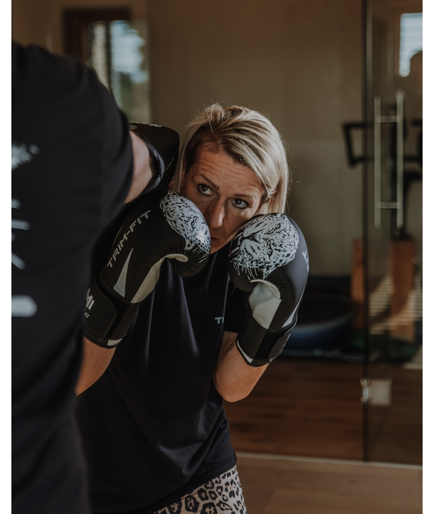 Eine Frau mit blonden Haaren boxt in einer Halle, trägt schwarze Handschuhe und konzentriert sich auf ihren Gegner.