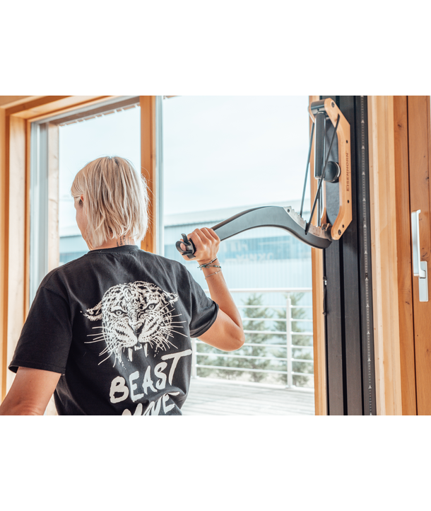 Person, die in einer Halle mit Widerstandsgeräten trainiert und ein BEAST MODE-Shirt mit einer Tigerdarstellung auf dem Rücken trägt.