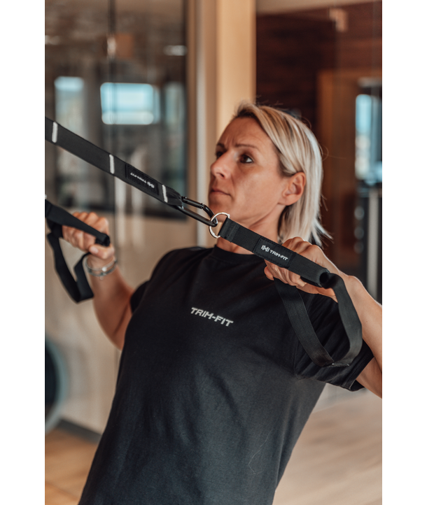 Frau, die in der Halle mit Aufhängebändern trainiert, trägt ein schwarzes TRAIN-FIT T-Shirt.
