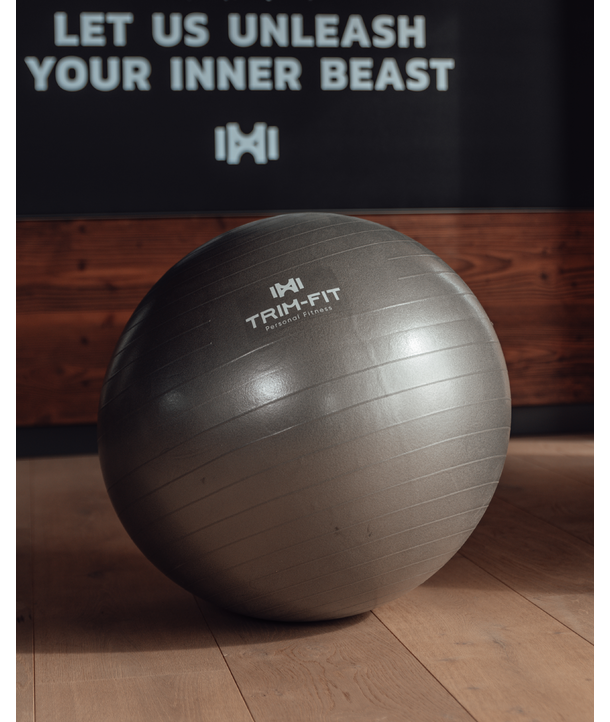 Ein grauer Gymnastikball liegt auf einem Holzfußboden, dahinter steht ein motivierender Text an der Wand.