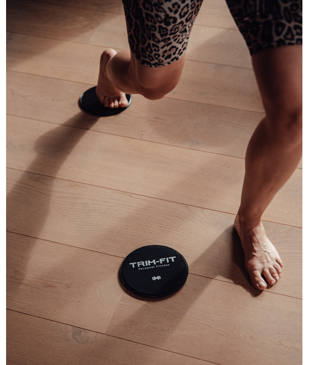 Person, die auf einem Holzboden mit TRIM-FIT-Schiebescheiben trainiert, in Sportshorts mit Leopardenmuster.