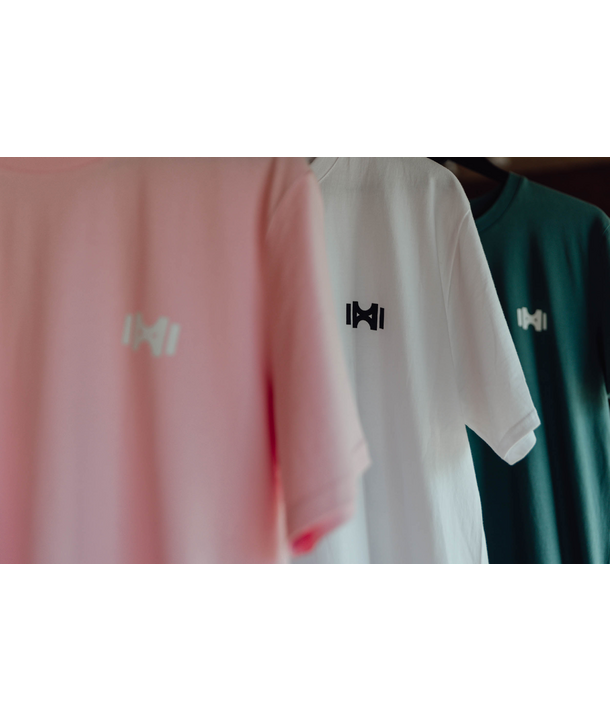 Drei T-Shirts in Rosa, Weiß und Grün mit minimalistischen Logos hängen an einem Ständer.