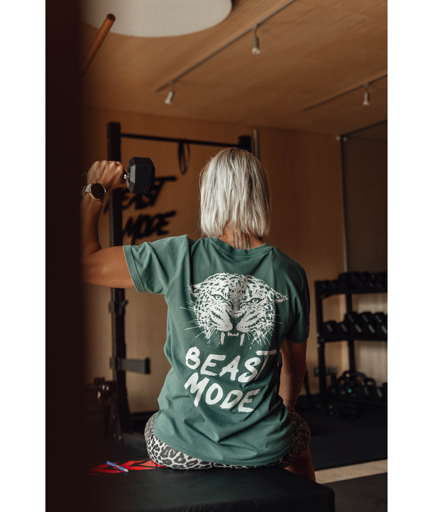 Person, die eine Hantel im Fitnessstudio hebt und ein grünes Beast Mode-Shirt mit einem Tigergesicht auf dem Rücken trägt.
