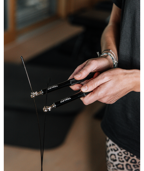 Person hält schwarze Trommelstöcke, trägt Armbänder und Hosen mit Leopardenmuster.