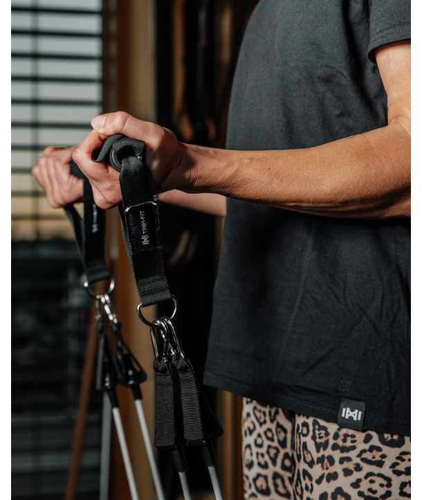 Person, die Griffe von Widerstandsbändern ergreift und ein dunkles Hemd und Leggings mit Leopardenmuster in einem Raum trägt.