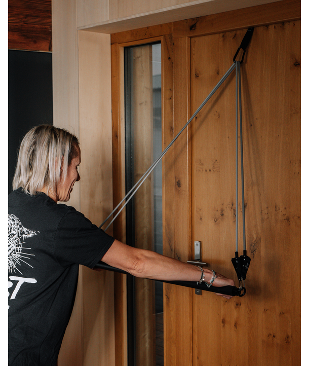 Person mit Widerstandsbändern, die an einer Holztür verankert sind, für eine Oberkörperübung in einem Raum.