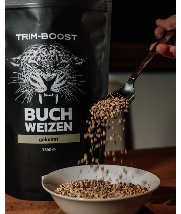 Eine Hand schüttet Buchweizengrütze in eine Schale vor einer Trim-Boost-Buchweizen-Verpackung.