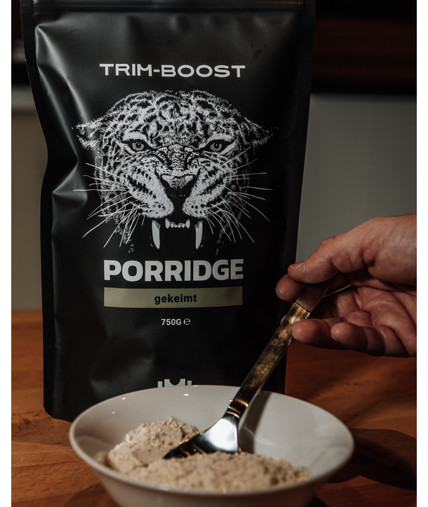 Eine Hand hält einen Löffel in einer Pulverschüssel mit einer Trim-Boost Porridge-Verpackung, auf der im Hintergrund ein Leopard abgebildet ist.
