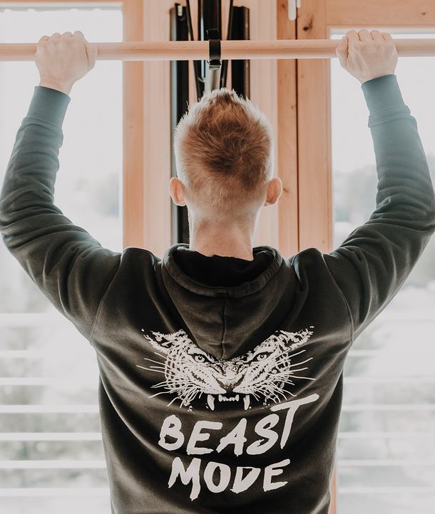 Person, die einen Klimmzug macht und einen Kapuzenpullover mit einem Tiger und der Aufschrift BEAST MODE auf dem Rücken trägt.