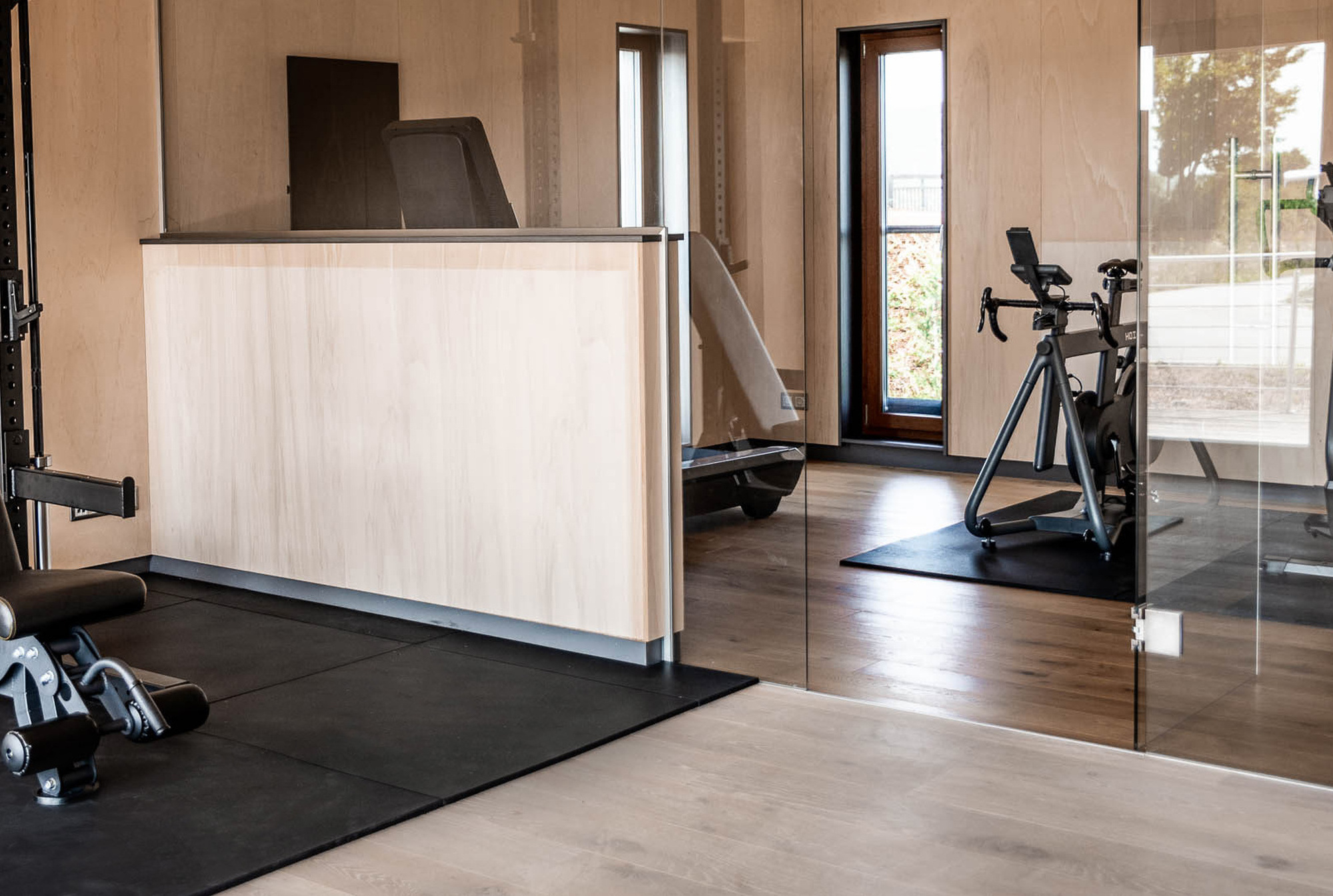 Modernes Fitnessstudio mit einer Bank, Hanteln, einem Heimtrainer und großen Fenstern für natürliches Licht.