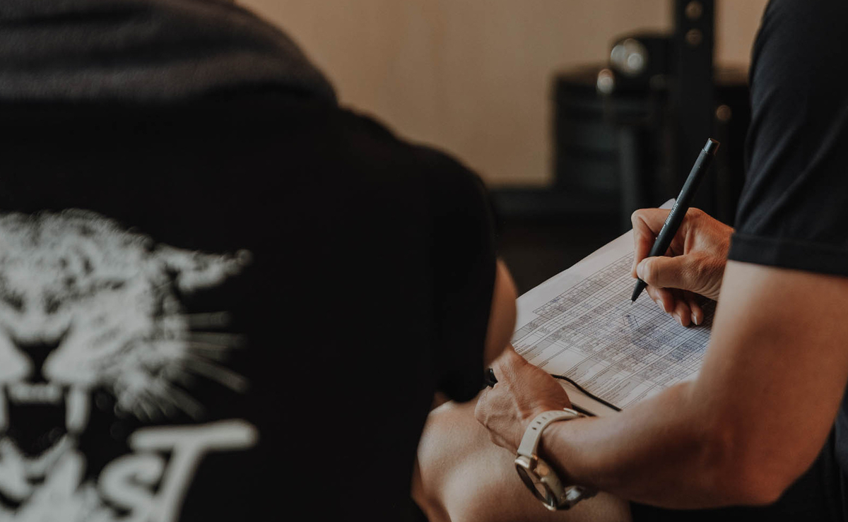 Zwei Personen überprüfen und füllen einen Trainingsplan in einem Fitnessstudio aus.