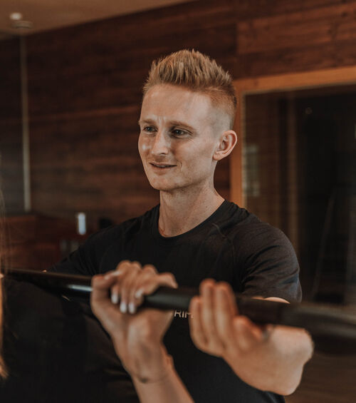Ein Mann in einem schwarzen Hemd hilft jemandem, eine Stange im Haus zu halten, lächelt und gibt Anweisungen.