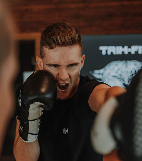 Mann in Boxhandschuhen, der einen Schlag in Richtung der Kamera ausführt, mit konzentriertem und intensivem Blick.