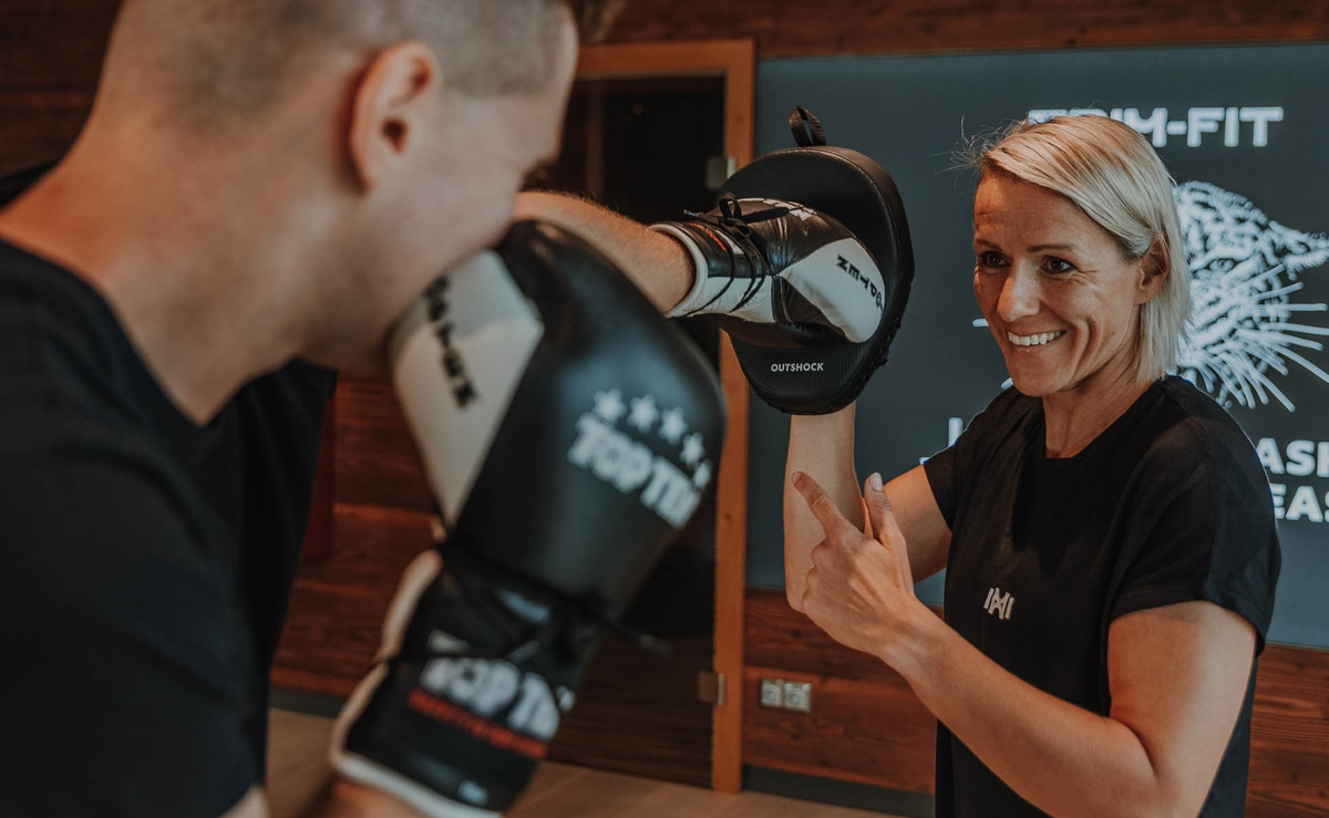 Eine Frau, die Boxhandschuhe trägt, lächelt, während sie mit einem Mann trainiert, der Boxhandschuhe in einem Haus trägt.