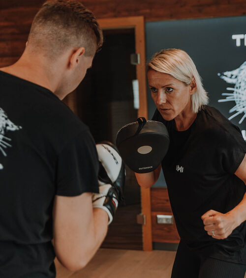 Zwei Personen beim Sparring in einer Halle, einer hält einen Fokus-Pad, während der andere einen Schlag ausführt, beide sehen konzentriert aus.