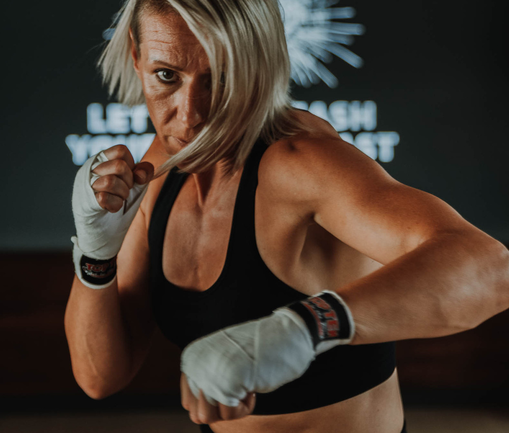 Eine zielstrebige Frau mit kurzen blonden Haaren, die einen Faustschlag ausführt, trägt Handschellen und einen schwarzen Sport-BH.
